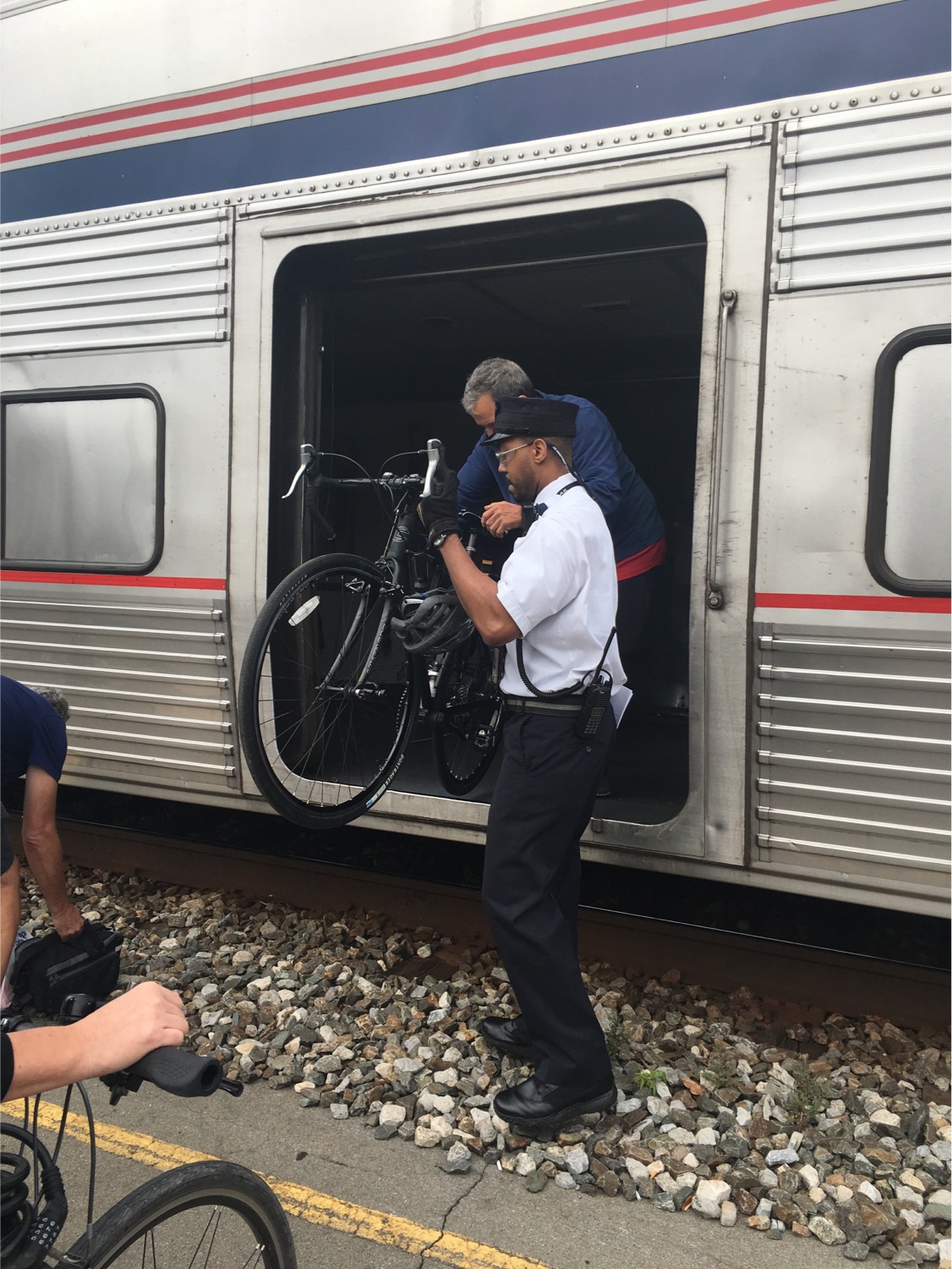 A train conductor helping a passenger lift a bicycle out of a train car